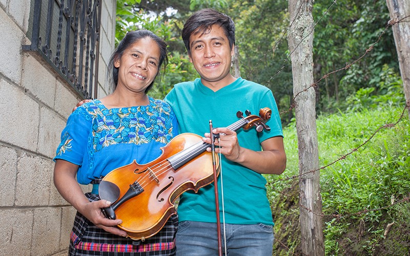 Tomasa et Gustavo tiennent tous les deux l’alto, à l’extérieur de leur maison au Guatemala.