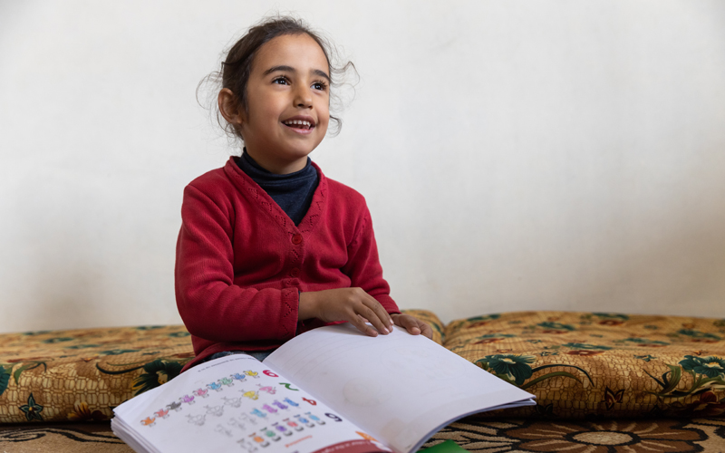 Une fillette libanaise tient un livre et affiche un large sourire.