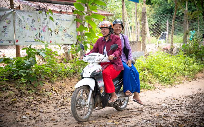 two women smile riding a motorcycle in Myanmar.