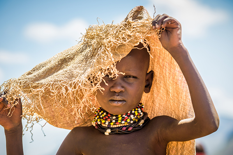 Une jeune fille se protège du soleil avec un sac servant à la distribution de nourriture.
