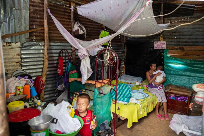 Une migrante vénézuélienne est assise sous sa tente avec deux de ses enfants.
