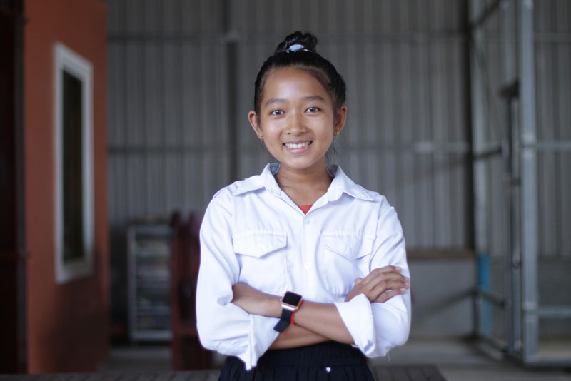 Une jeune fille portant une chemise blanche se tient avec les bras croisés et souriant pour la photo.