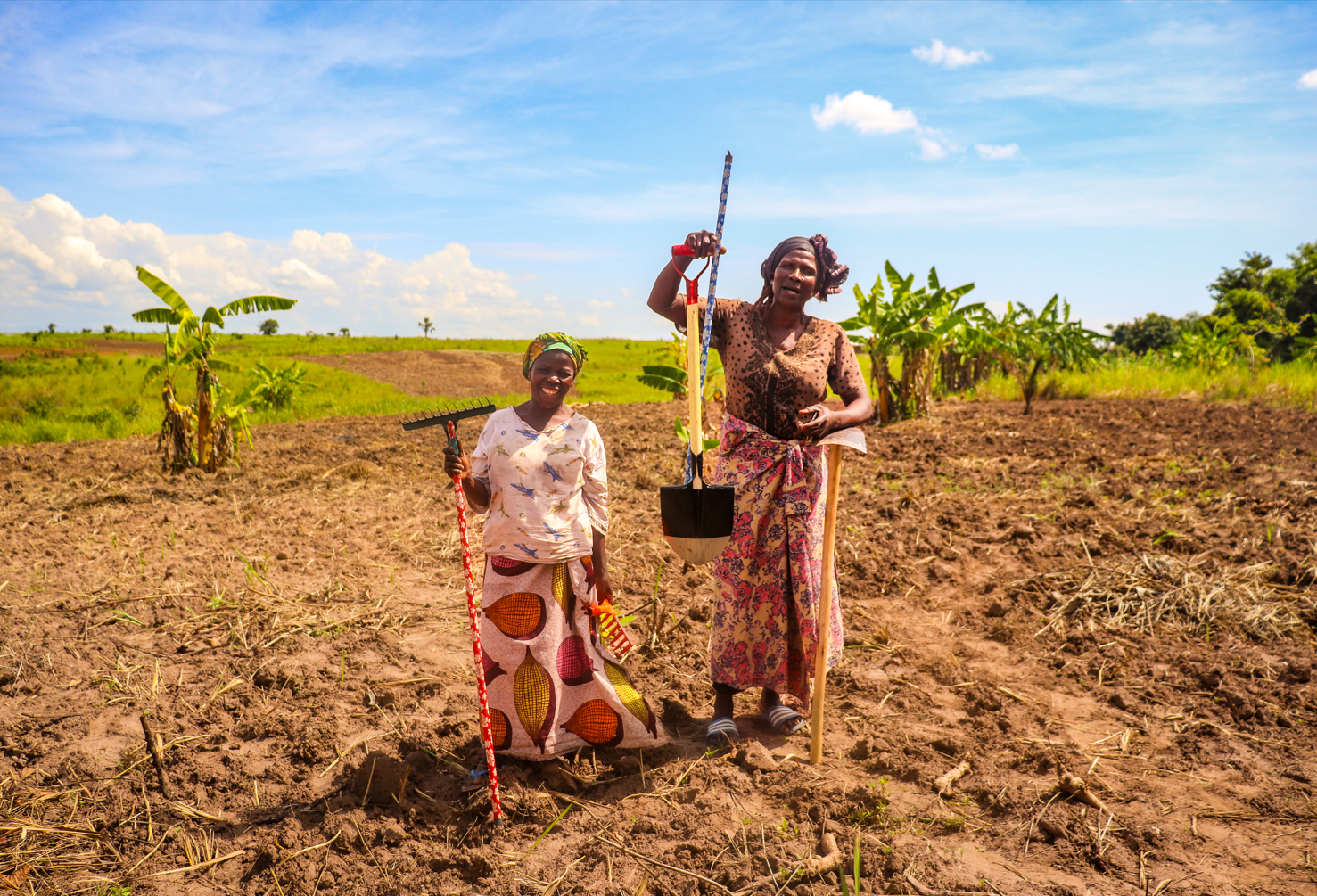 Deux femmes tiennent chacune un outil agricole et sourient. 