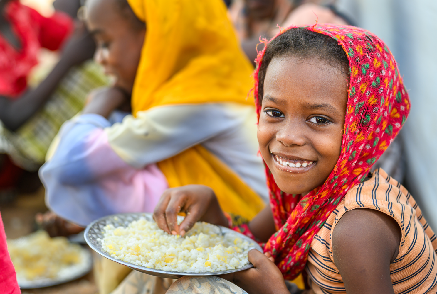 Une enfant sourit en tenant une assiette de nourriture fournie par le programme d’alimentation scolaire de Vision Mondiale.