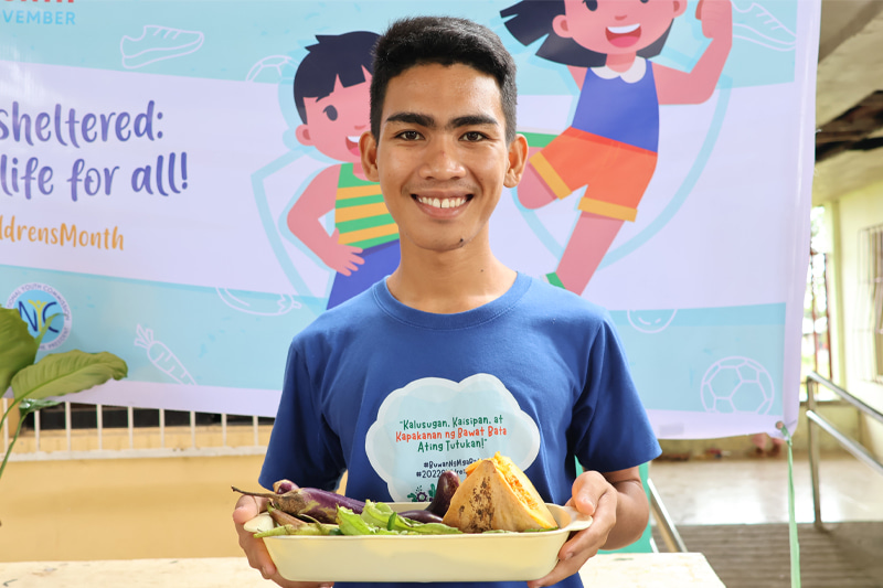 Un adolescent philippin porte un haut bleu et tient un bol de légumes.