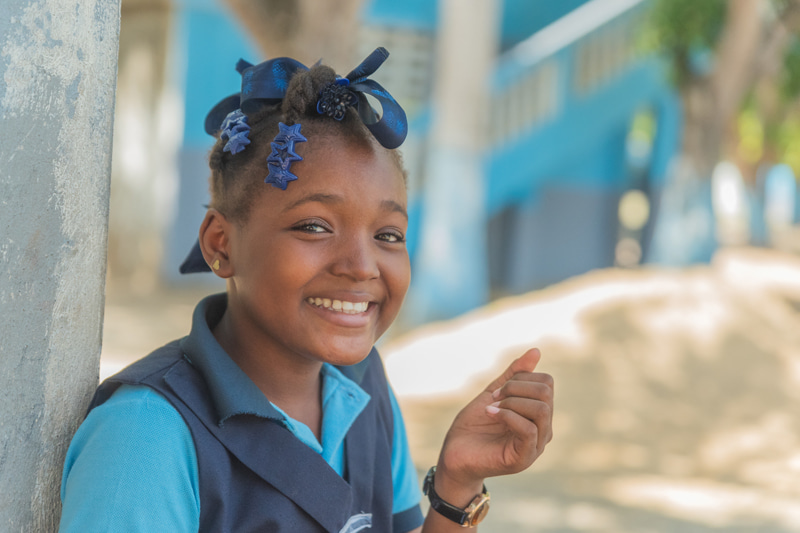 Une jeune fille portant un uniforme scolaire bleu sourit à l’objectif.