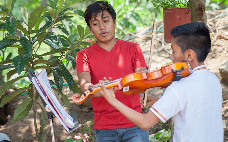 Gustavo enseigne à un jeune élève à jouer les bonnes notes sur le violon.