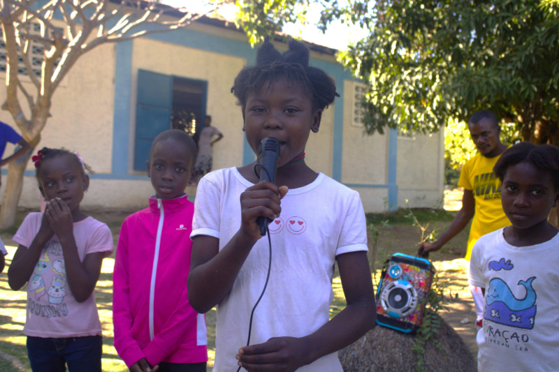 Une jeune fille parle dans un microphone tandis que d’autres enfants se tiennent autour d’elle.