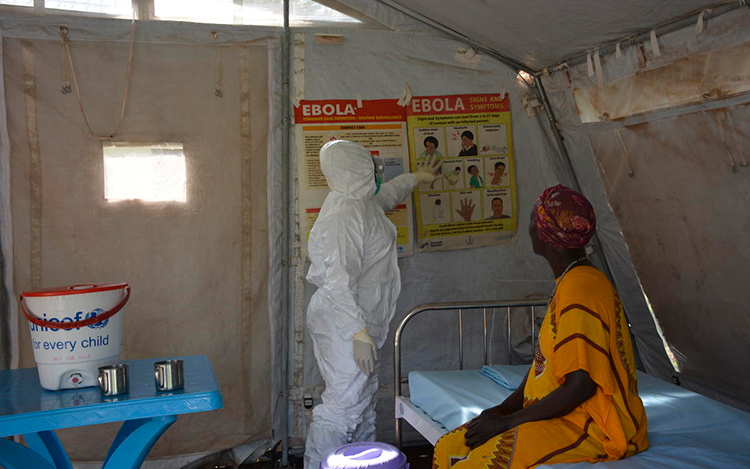 Vêtue d’une combinaison contre les matières dangereuses, une femme donne des informations à une patiente dans un centre de santé du Soudan du Sud.